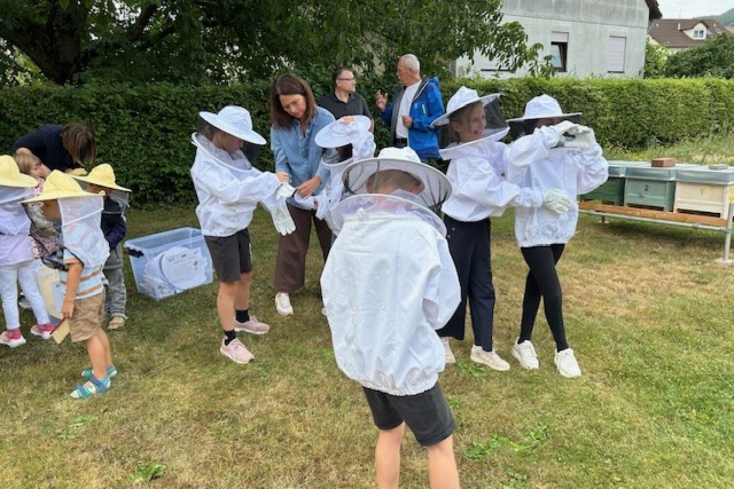 Kinder auf einer Wiese beim Anziehen von Imkerausrüstung.