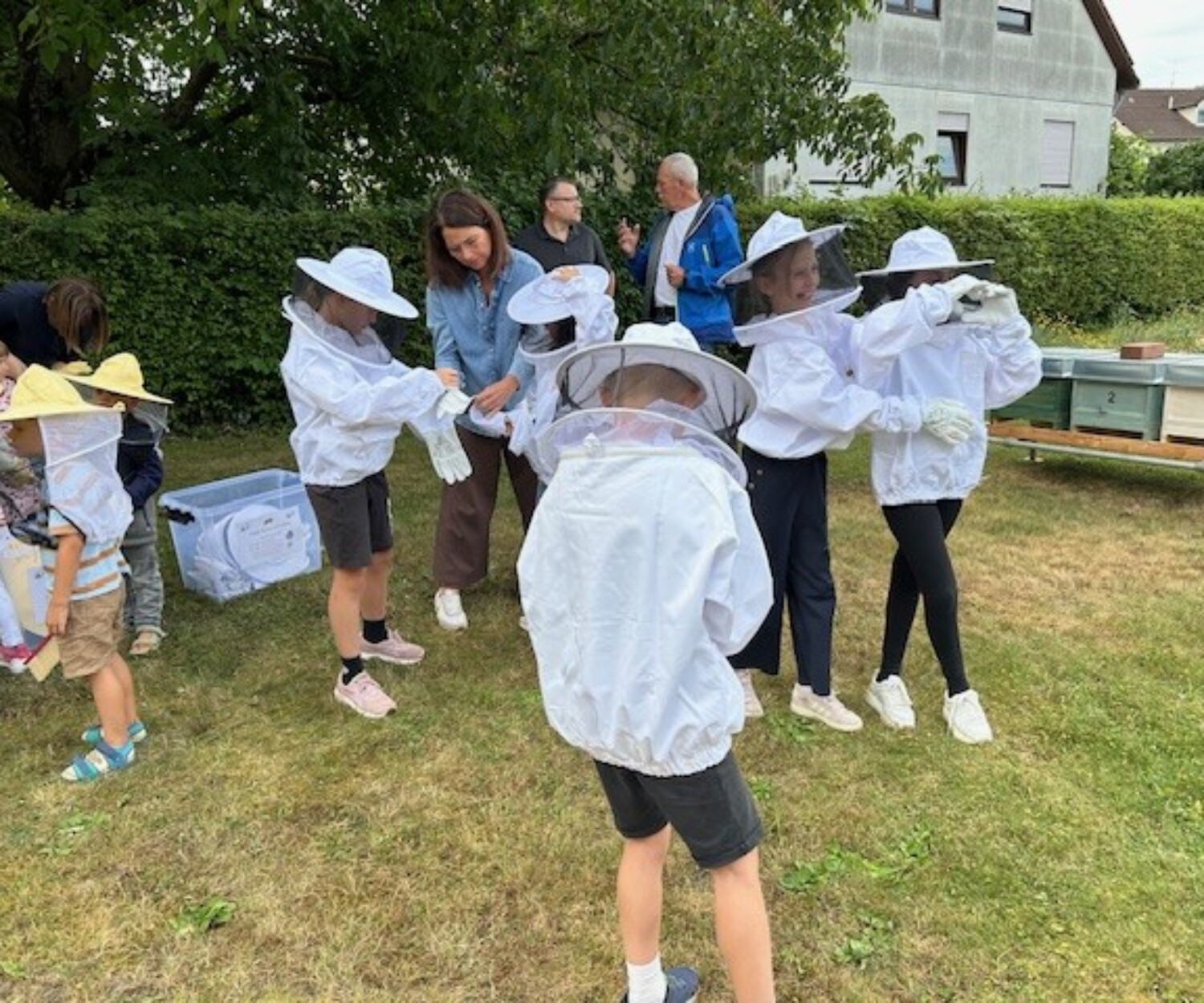 Kinder auf einer Wiese beim Anziehen von Imkerausrüstung.